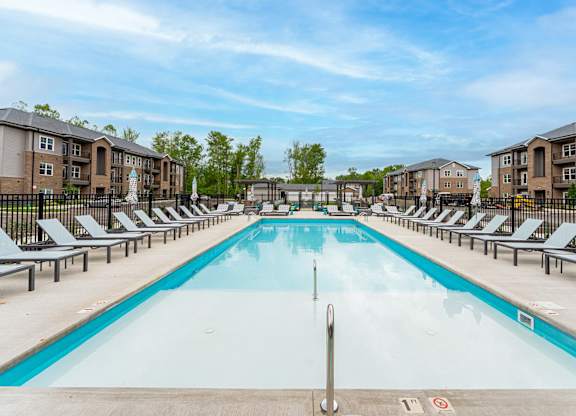 A large swimming pool surrounded by sun loungers and apartment buildings.