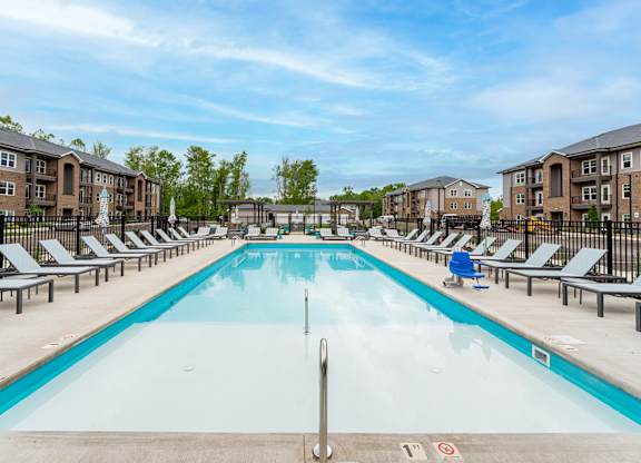 A large swimming pool surrounded by sun loungers and apartment buildings.