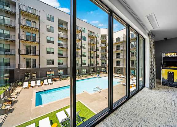 A view from inside a building looking out to a pool and sun loungers.