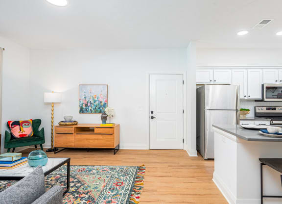 a living room with a kitchen with a refrigerator and a microwave