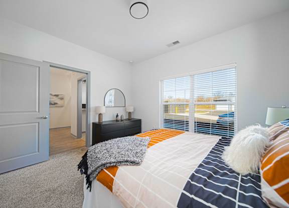 A bedroom with a bed, a nightstand, and a window with blinds.