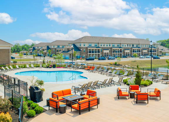 an outdoor pool with orange chairs and tables and a building in the background
