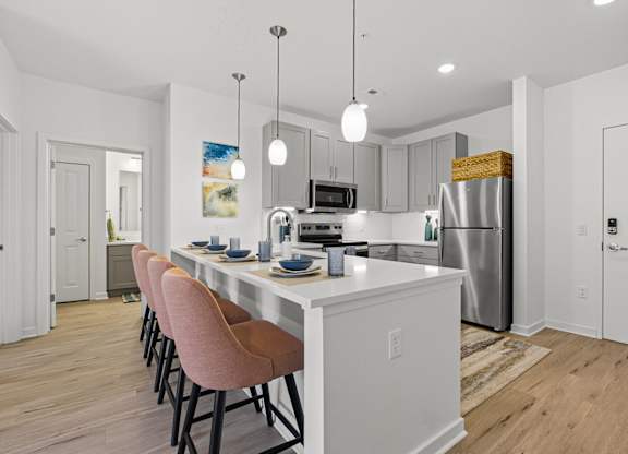 A kitchen with a white island and pink chairs.