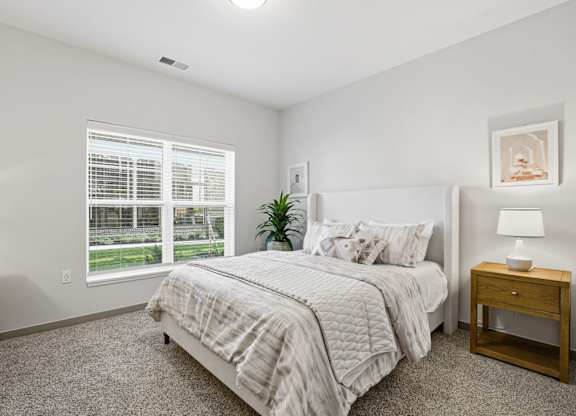 A bedroom with a bed, nightstand, and window.
