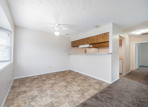 an empty living room with a kitchen area and a ceiling fan