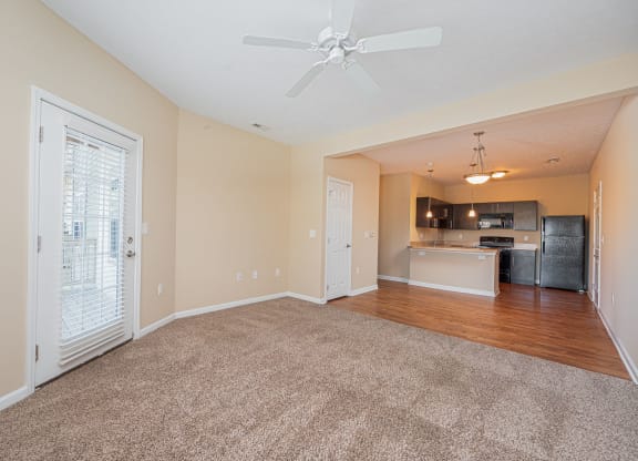 an empty living room with a ceiling fan and a kitchen