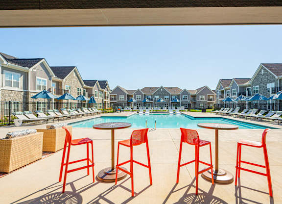 A pool surrounded by red chairs and tables.
