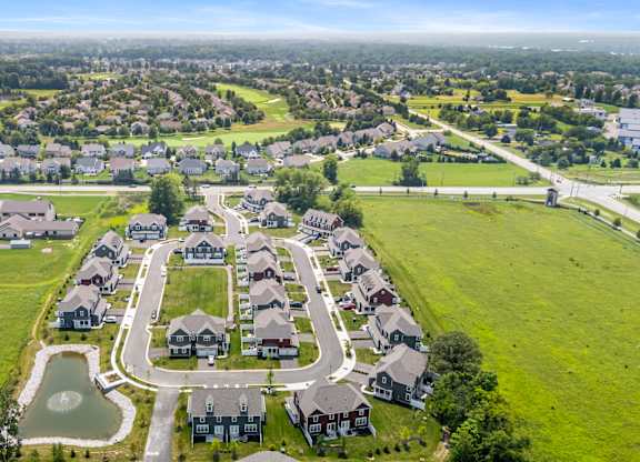 A bird's eye view of a residential area with houses and a pond.
