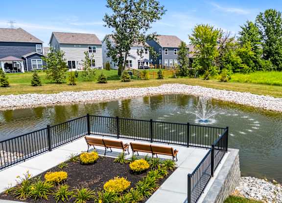 A pond with a bench and a fence in the foreground with houses in the background.