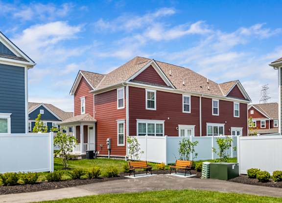 A red house with white fence and green bushes in front.