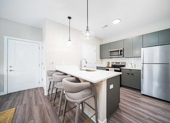 A kitchen with a white island and grey chairs.