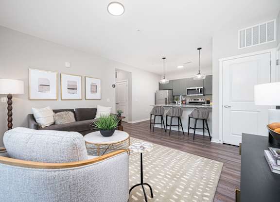 A modern living room with a grey sofa and a kitchen area in the background.