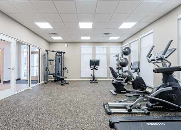 A spartan room with a treadmill, weights and exercise equipment.