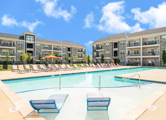 a swimming pool with lounge chairs in front of an apartment building