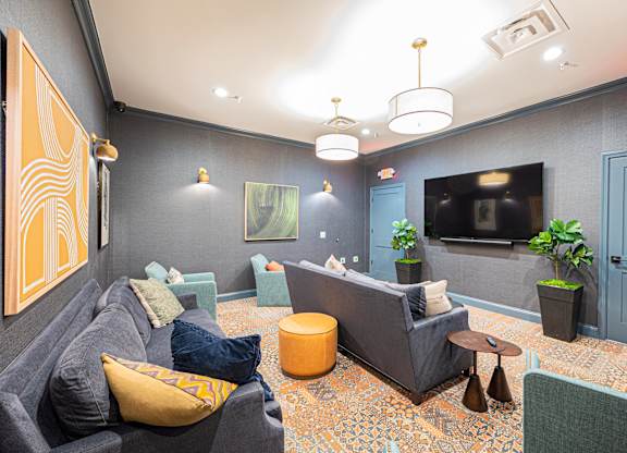 A living room with a grey couch, a yellow pillow, and a TV on the wall.