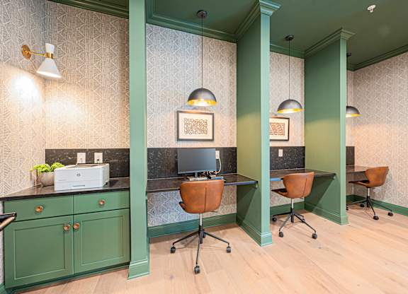 A room with green walls and wooden floors has a desk with a computer and a chair.