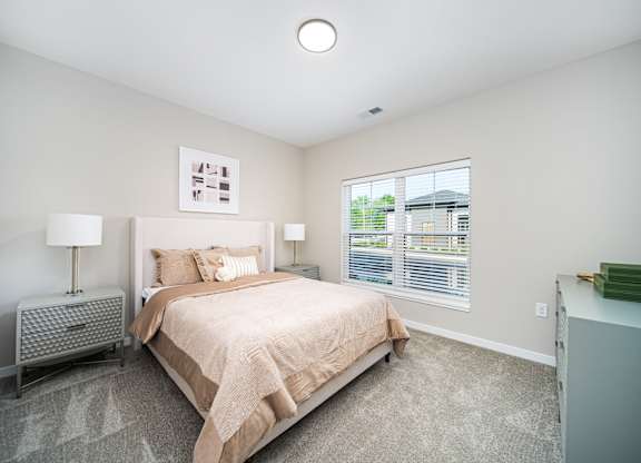 A bedroom with a large bed and a window with blinds.