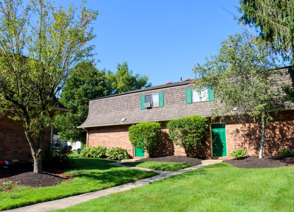 a brick house with green doors and a lawn