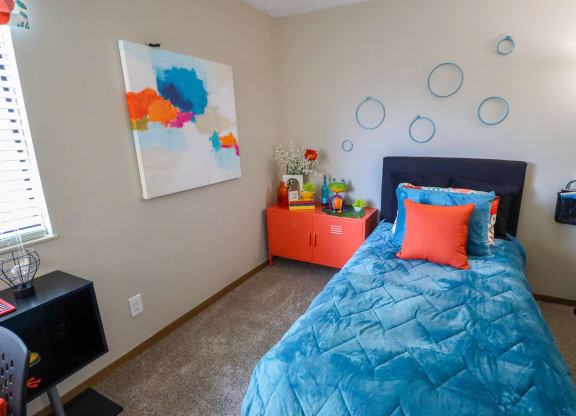 A bedroom with a blue comforter and a painting on the wall.