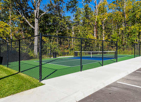A tennis court surrounded by a black fence and trees.