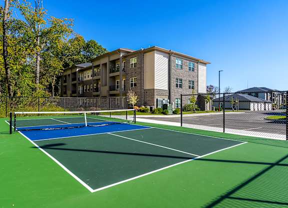 A tennis court is surrounded by apartment buildings.