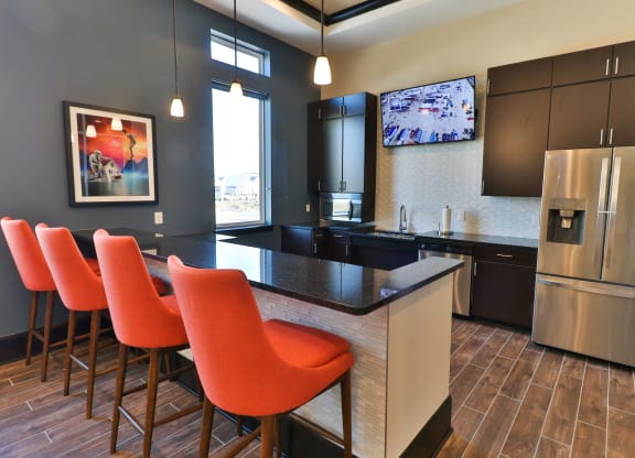 a kitchen with a bar with orange chairs and a stainless steel refrigerator