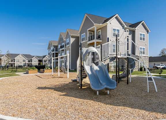 A playground with a slide and swings in front of apartment buildings.