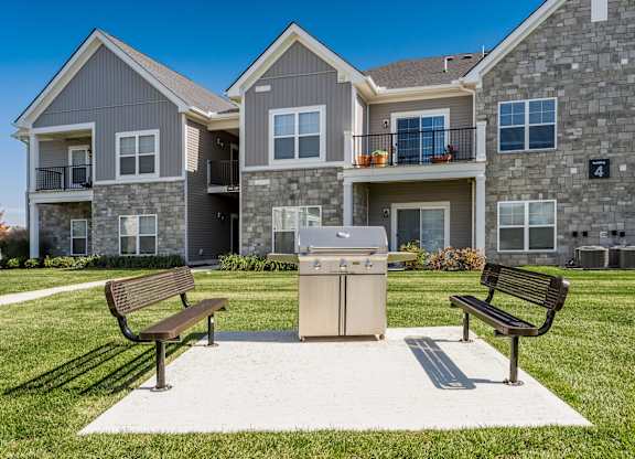 A large house with a grey and brown exterior has a small patio with two benches and a trash can.