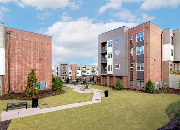 A modern apartment complex with a grassy courtyard and a bench.