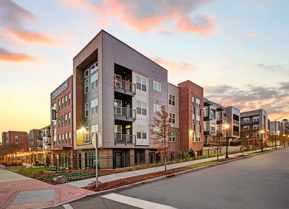 Apartment buildings are shown in the evening with lights on.