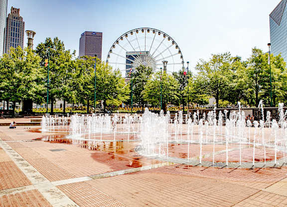 A fountain in the middle of a square with a Ferris wheel in the background.