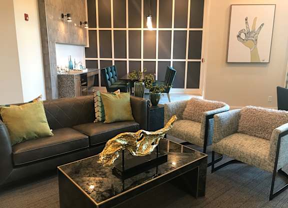 A living room with a black couch, a coffee table, and a painting on the wall.