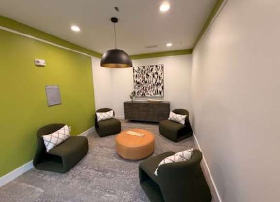 A room with green walls and grey carpet has a large brown ottoman in the middle.
