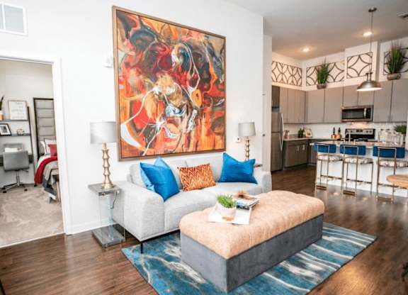 A living room with a large painting on the wall and a white couch with blue pillows.
