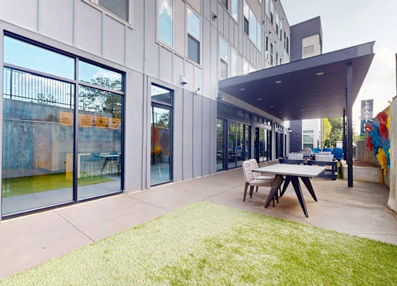 A modern patio with a table and chairs is surrounded by a grassy area.