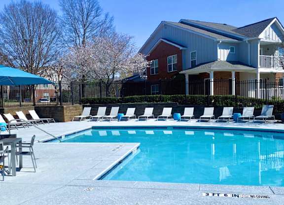 A swimming pool in front of a house with a fence and trees in the background.