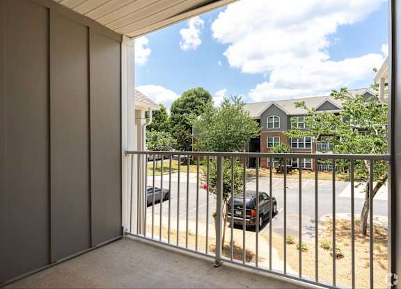 A balcony with a metal railing overlooks a parking lot and a building.