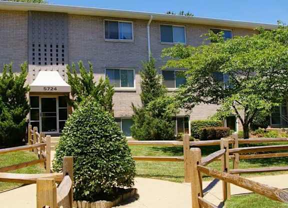 A building with the number 6724 on it is surrounded by a wooden fence and green trees.