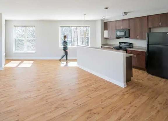 A person is walking in a spacious kitchen with wooden floors and white walls.