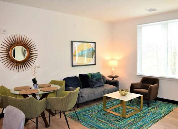 A living room with a grey couch, green chairs, a wooden coffee table, and a large mirror on the wall.