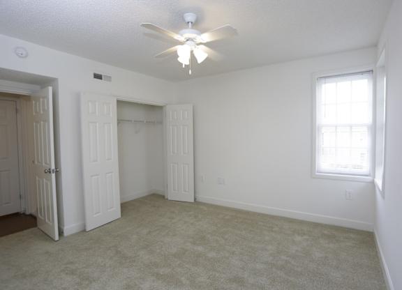 an empty living room with a ceiling fan and a closet