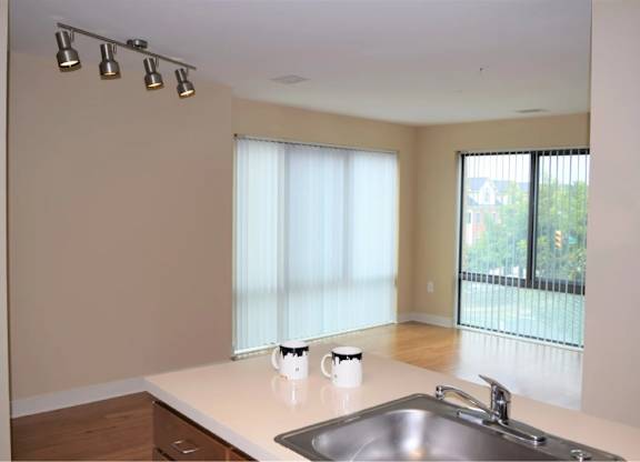 A kitchen with a sink, a window with blinds, and a white countertop.