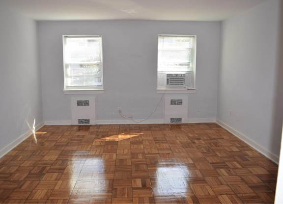 A room with wooden flooring and two windows.