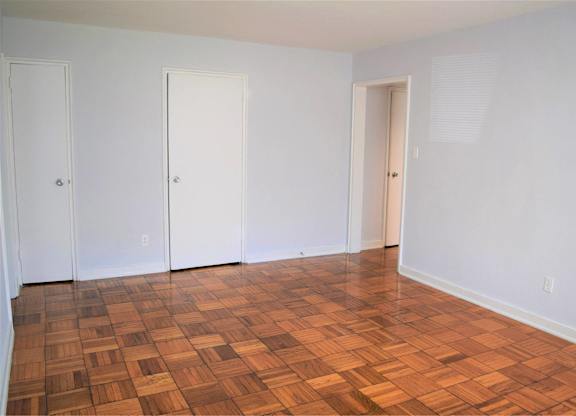 A room with white walls and a wooden floor with four doors.