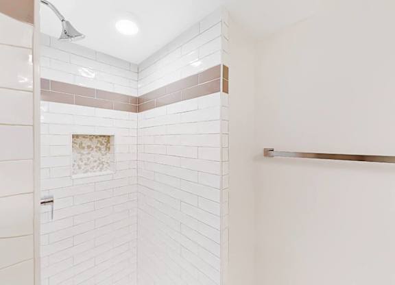 A white tiled shower with a brown tile border and a white towel bar.