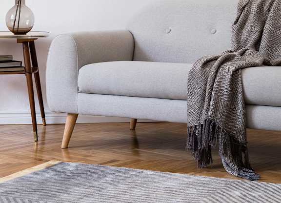 A grey couch with a grey blanket on it.