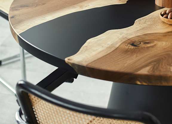 A round wooden table with a bowl of green fruit and a vase with a plant on it.