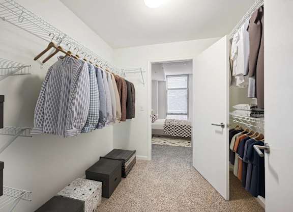 A walk in closet with clothes hanging and drawers underneath.