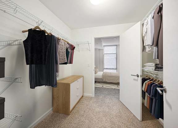 A walk in closet with clothes hanging and a bench.
