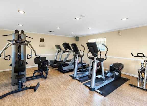 A gym with a variety of equipment including treadmills, stationary bikes, and weight machines. at The Oaks Apartments, Upland